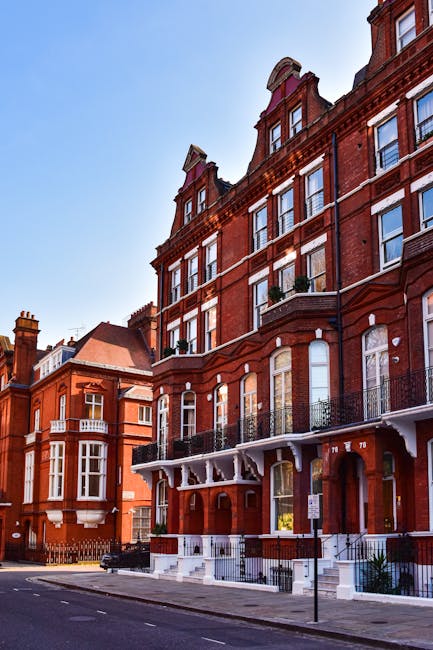 A three-storey Victorian-style house with a yellow brick facade and white decorative trim around the windows and entrance, situated on a residential street under a clear blue sky. The front garden fea